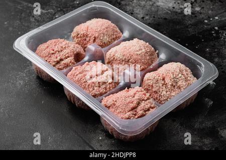 Boulettes de dindon crues dans un plateau jetable en plastique, sur fond noir de table en pierre sombre Banque D'Images