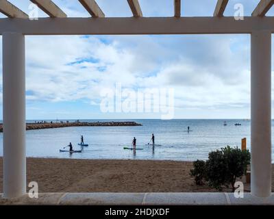 Vue depuis une pergola sur la promenade de bord de mer de certains surfeurs pratiquer leur sport préféré dans les eaux du port de Fuengirola sur une silex nuageux Banque D'Images