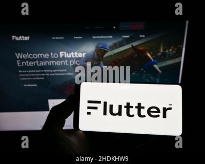 Personne tenant un smartphone avec le logo de la société de librairie irlandaise Flutter Entertainment plc à l'écran devant le site Web.Mise au point sur l'affichage du téléphone. Banque D'Images