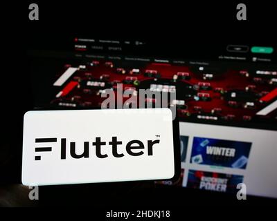 Personne tenant un téléphone portable avec le logo de la société de bookmaking Flutter Entertainment plc à l'écran devant le site de Pokerstars.Mise au point sur l'affichage du téléphone. Banque D'Images