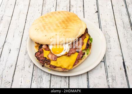 Hamburger sauvage aux œufs frits typiques, lanières et tranches de bacon et de cheddar et beaucoup de laitue Banque D'Images