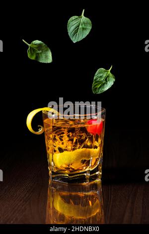Prise verticale d'un whisky avec zeste dans un verre et de feuilles vertes sur fond sombre Banque D'Images