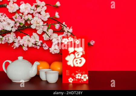 Paquet d'enveloppe rouge ou ang bao (mot mean Wealth) met avec thé set et des oranges qui ont la fleur de pêche sur fond de papier rouge pailleté. Banque D'Images