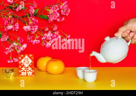 Thé versé à la main de pot pour le nouveau concept chinois de l'année avec des oranges, enveloppe rouge ou ang bao (mot signifie grande fortune) et des lingots sur le jaune et rouge gl Banque D'Images