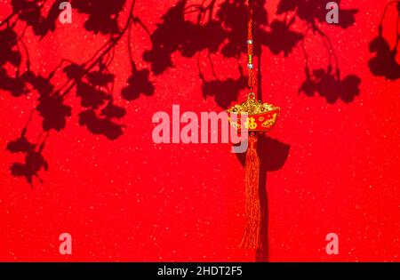 Pendentif suspendu (mot mean Wealth) pour décoration chinoise du nouvel an avec ombre de fleurs de pêche sur fond de papier brillant rouge. Banque D'Images