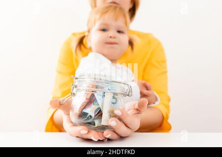 Mère tient un pot en verre rempli d'argent.L'enfant regarde la berge.Gros plan des mains et du bol.Le concept de l'investissement et de l'assurance. Banque D'Images