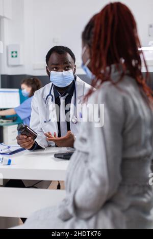 Médecin tenant une bouteille de pilules à la patiente enceinte dans le cabinet médical.Patient attendant bébé recevant un ballon avec un médicament sur ordonnance et un traitement par un médecin, portant un masque facial Banque D'Images