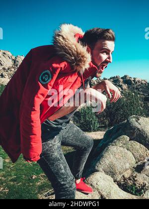 Un homme de race blanche avec une veste rouge qui se camout comme un dinosaure dans les collines Banque D'Images