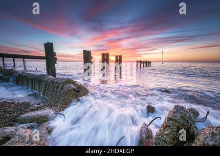 Bawdsey au lever du soleil avec des vagues s'écrasant à travers les vieilles défenses maritimes, Suffolk UK Banque D'Images