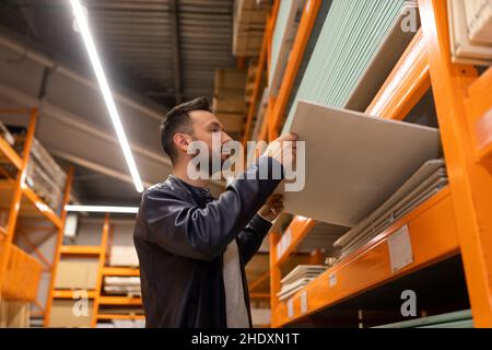 Un homme dans une hypermarché de construction choisit des matériaux pour la décoration de mur examine les panneaux OSB et les panneaux de particules de ciment Banque D'Images