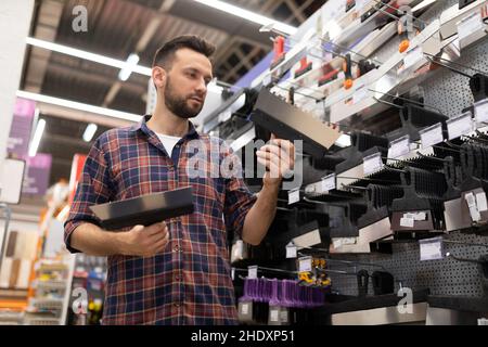 Un homme Un acheteur de constructeur dans un hypermarché de construction achète des spatules pour le putilier, un concept de finition avec le plâtre et le putty, un choix d'outils pour Banque D'Images