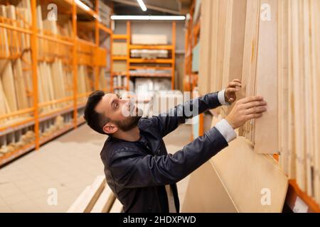 un homme dans un supermarché de construction choisit le contreplaqué et les panneaux pour la construction, le concept d'armement ménager et la construction d'un bâtiment résidentiel. Banque D'Images