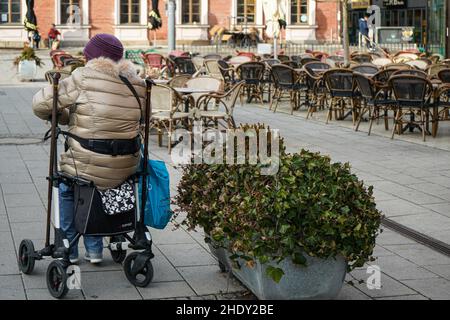 Une femme ayant un handicap de marche repose sur son marcheur à côté d'un restaurant extérieur vide. Banque D'Images