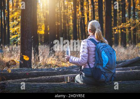 Détente en forêt pendant la randonnée automnale.Femme voyageur avec sac à dos tenant un thermos Banque D'Images