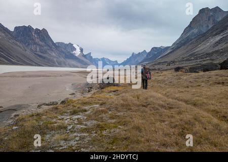 Randonneur avec un sac à dos lourd marchant dans une vallée arctique isolée par une journée nuageux. Paysage arctique spectaculaire du col Akshayuk, île de Baffin, Canada. Mt Banque D'Images