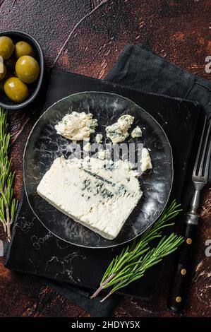 Coin de fromage Roquefort dans une assiette d'acier avec des olives et des herbes.Arrière-plan sombre.Vue de dessus Banque D'Images