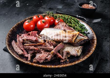 Côtelettes de bœuf fumées et grillées dans une assiette rustique aux herbes.Arrière-plan noir.Vue de dessus Banque D'Images