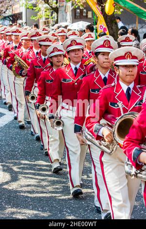 Des rangées de membres du groupe d'adolescents japonais de la bande de Waseda, en uniformes de style militaire rose et blanc marchant vers le spectateur dans une procession. Banque D'Images