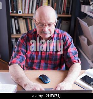 Homme senior avec lunettes avec ordinateur portable à la maison recherchant sur Internet Banque D'Images