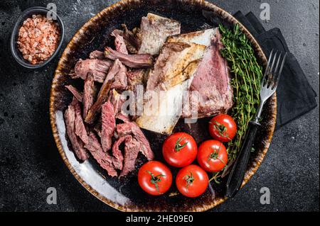 Côtelettes de bœuf fumées et grillées dans une assiette rustique aux herbes.Arrière-plan noir.Vue de dessus Banque D'Images