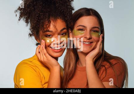 JOURNÉE AU SPA.Deux filles multiraciales avec des taches d'oeil près l'une de l'autre joue à joue, souriant agréablement avec les yeux fermés, amies heureux appréciant sk Banque D'Images