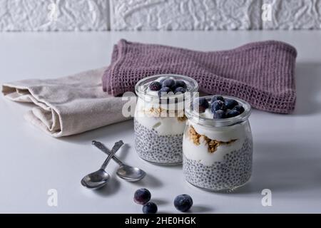 Graines de Chia au yaourt recouvertes de bleuets congelés sur table blanche Banque D'Images