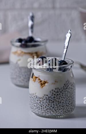 Graines de Chia au yaourt recouvertes de bleuets congelés sur table blanche Banque D'Images