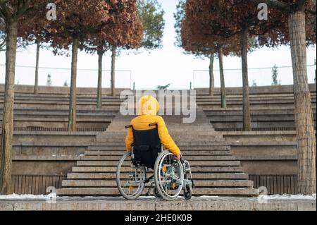 Femme en fauteuil roulant devant les escaliers dans la rue en hiver. Banque D'Images