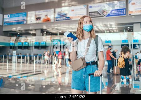 Bonne jeune femme touristique dans un masque médical de protection portant un passeport à l'aéroport international.Voyager après la pandémie Covid-19 Banque D'Images