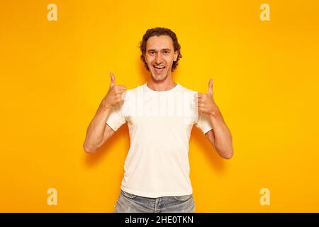jeune homme excité en vêtements décontractés montre les pouces avec les deux mains avec sa bouche ouverte bonheur. isolé fond jaune. espace pour le texte. concept - personnes, bonnes nouvelles, promotions, rabais, aime.Photo de haute qualité Banque D'Images