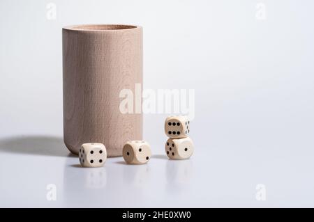 Gros plan de quatre dés contre une tasse en bois isolée sur un fond blanc Banque D'Images