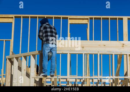 Gros plan d'un travailleur dans des gants de protection blancs tenant une planche l'installant sur la construction de ménage à l'aide d'un marteau pneumatique dans des poutres en bois clouant. Banque D'Images