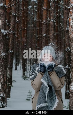 la fille souffle de la neige de ses mains.Une fille dans un chapeau jette de la neige dans la forêt d'hiver.Joyeuses vacances d'hiver.Amour pour l'hiver.Hiver dans le nord. Banque D'Images