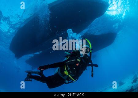 Un plongeur passe sous des bateaux amarrés dans les eaux claires de la mer Rouge au large de la côte d'Hurghada, en Égypte. Banque D'Images