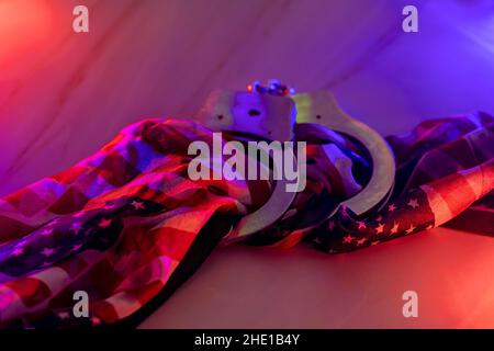 La police est en état d'arrestation de menottes et les feux de police rouges et bleus clignotent sur fond de drapeau américain Banque D'Images