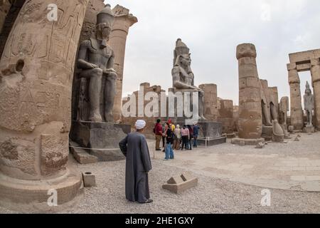 Des touristes et un homme local se tiennent sous des statues massives de Ramses II au temple de Louxor, un site archéologique en Égypte. Banque D'Images