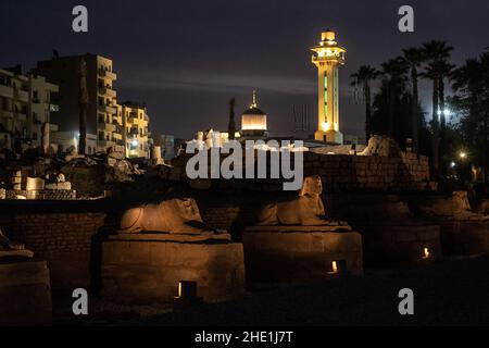Des statues Sphinx bordent la route des béliers à Louxor, en égypte, avec la ville et illuminent le minaret en arrière-plan. Banque D'Images