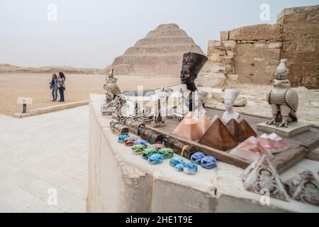 Divers bibelots à vendre pour les touristes avec la pyramide Saqqara STEP de Djoser en arrière-plan, le plus ancien bâtiment de pierre connu.Situé en Égypte. Banque D'Images