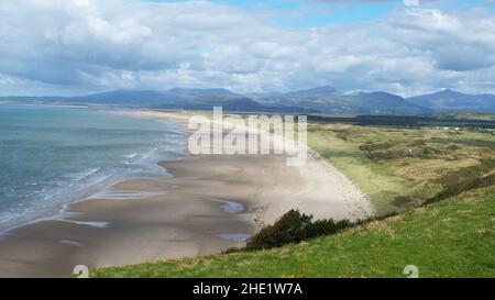Vaste plage de sable Harlech avec des vagues douces et des dunes herbeuses, soutenue par des montagnes lointaines sous un ciel partiellement nuageux, Gwynedd, pays de Galles, Royaume-Uni. Banque D'Images