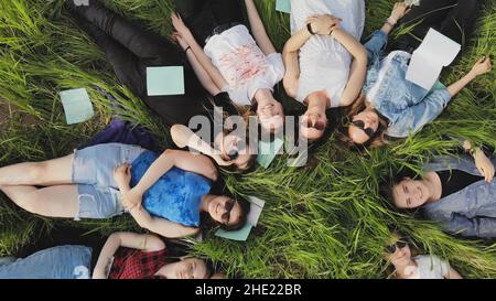 Les jeunes filles s'étendent sur l'herbe dans un parc de la ville avec des carnets. Banque D'Images