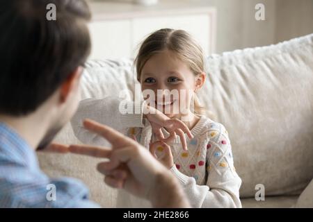 Bonne petite fille utilisant le langage des signes, communiquant avec le père. Banque D'Images