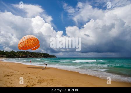 Parachute orange ouvert sur la plage en Thaïlande.L'homme propose d'aller pour une balade en parachute. Banque D'Images