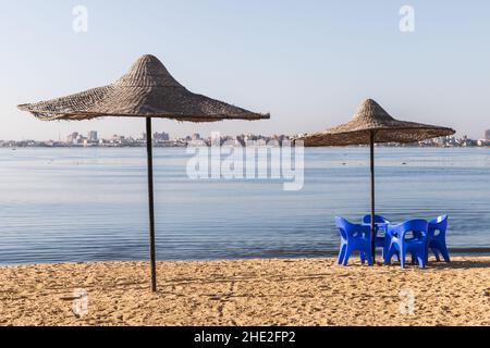 Des parasols en paille et des chaises en plastique bleu se trouvent sur la plage du lac Timsah, l'un des lacs amers reliés par le canal de Suez.Ismailia, Égypte Banque D'Images