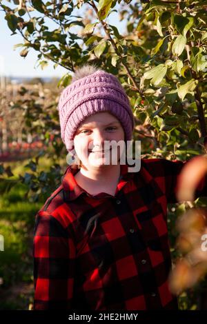 un jeune enfant portant un écossais rouge et noir et une casquette sourit dans un verger de pomme Banque D'Images
