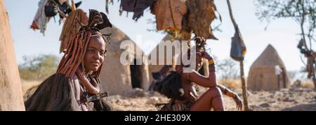 Photo panoramique montrant des femmes Himba assis à l'extérieur de leurs huttes dans un village Himba traditionnel près de Kamanjab dans le nord de la Namibie, en Afrique. Banque D'Images