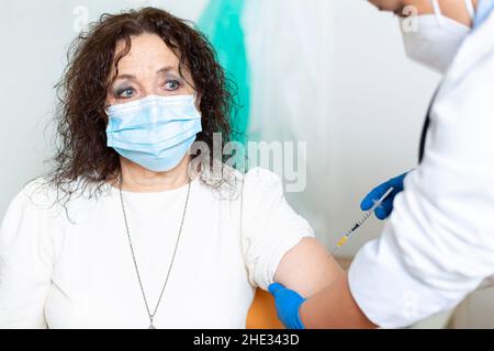 Une femme caucasienne plus âgée avec un masque facial étant vaccinée par un professionnel de la santé.Campagne de vaccination contre le virus Covid-19. Banque D'Images