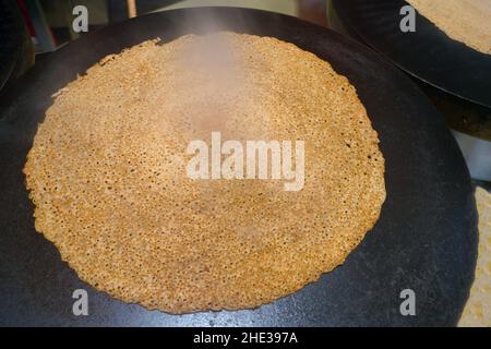 Une galette de sarrasin cuisinant sur une plaque de crêpe traditionnelle en Bretagne, en France Banque D'Images