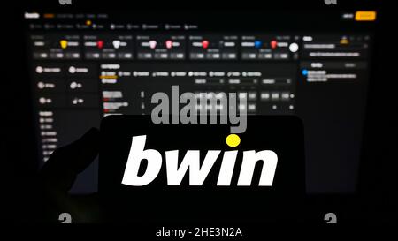 Personne tenant un smartphone avec le logo de la société autrichienne bwin Interactive Entertainment AG à l'écran devant le site Web.Mise au point sur l'affichage du téléphone. Banque D'Images