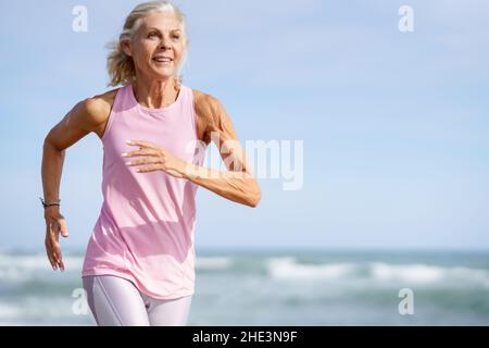 Une femme plus âgée fait du sport pour rester en forme.Femme d'âge mûr qui court le long de la plage. Banque D'Images