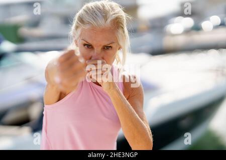 Femme mature qui fait de la boxe à l'ombre à l'extérieur.Femme senior faisant du sport dans un port côtier Banque D'Images